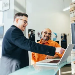 Man pointing at something on laptop, showing another man
