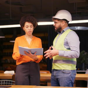 Male project manager discussing building plan with female engineer in hard hat and safety vest, concluding their successful meeting, handshake in modern office.